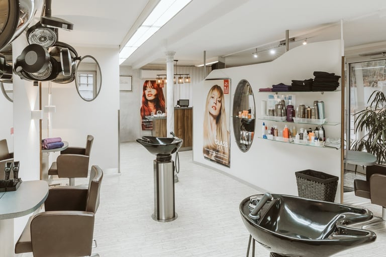 Modern hair salon interior with styling stations, mirrors, client chairs, and product displays on white walls