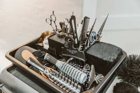 Professional hairstyling tools organized in a black holder, including scissors, combs, and brushes on a white surface