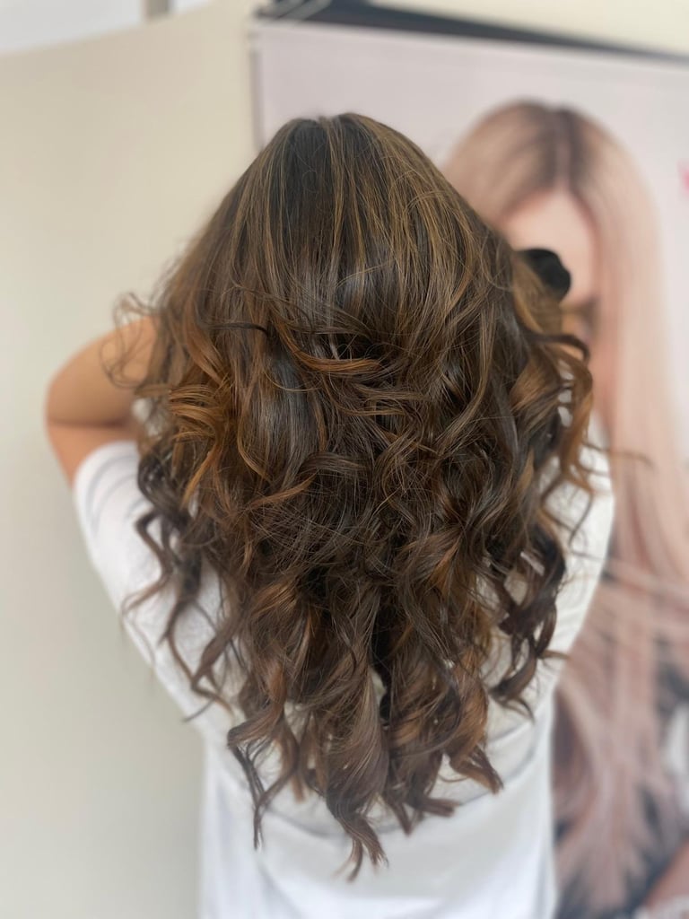 Woman with long, layered brunette hair with subtle caramel highlights and waves, shown from behind