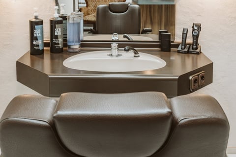 Modern bathroom sink with bronze countertop, white circular basin, chrome faucet, and grooming products displayed above a padded leather bench seat